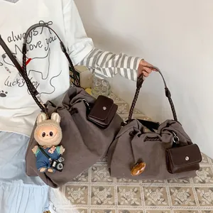 Large brown canvas drawstring tote bag with woven strap and small pendant accessory