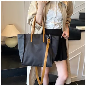 Detail of a black nylon tote bag featuring brown leather handles and a long shoulder strap