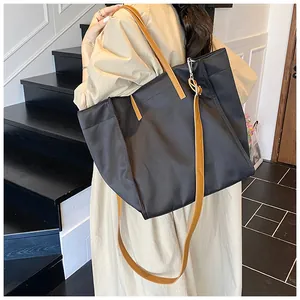 Large black nylon tote bag with brown straps worn by a model on a staircase