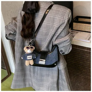 Detail of half-moon underarm bag with denim texture and teddy bear plush charm