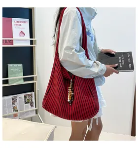 Detailed view of red and black striped knit tote bag with multicolor beaded pendant