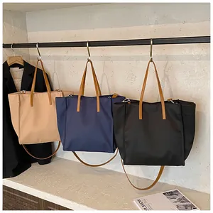 Three nylon tote bags in beige navy and black hanging on a rack with leather handles