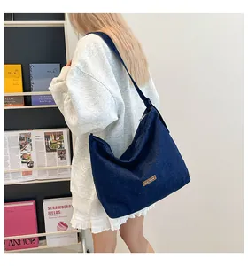 Dettaglio della grande borsa tote in denim blu scuro con etichetta in pelle sulla spalla