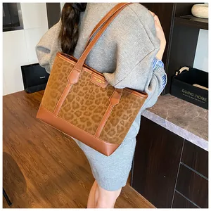 Detail of a leopard print tote bag with brown leather straps and gold-tone logo plaque
