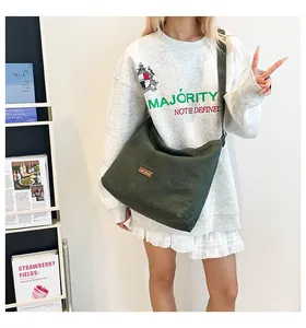 Dettaglio della borsa a tracolla in tela verde scuro con patch logo in pelle marrone su modella