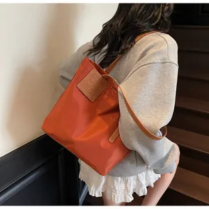 Detail van oranje nylon tote bag met bruine leren riemen en logo-patch op de zijkant