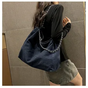 Detail of blue denim tote bag with silver chain strap and drawstring closure shown on model