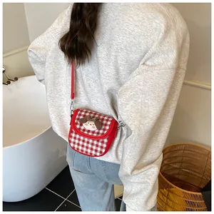 Detail of red and white checkered crossbody bag with cute cartoon doll on a model