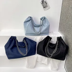 Three chain denim tote bags in black and blue shown on a modern white tiered display