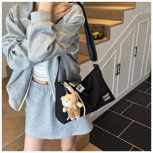 Détail du sac messager en toile noire avec broderie cœur rose et peluche d'ours mignonne