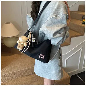 Détail du sac messager en toile noire avec logo brodé rose et breloque ours en peluche