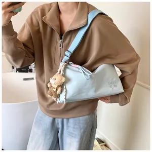 Détail de la sacoche bleu clair avec large bandoulière, ours en peluche et logo brodé