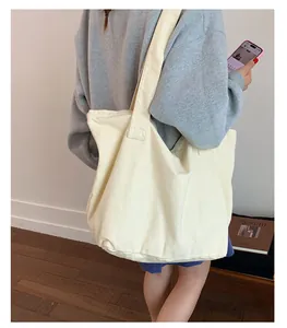 Détail d'un grand sac cabas en toile crème porté à l'épaule par un mannequin dans un décor épuré