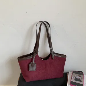 Detail of burgundy suede tote bag showing contrast brown leather straps and metal buckles
