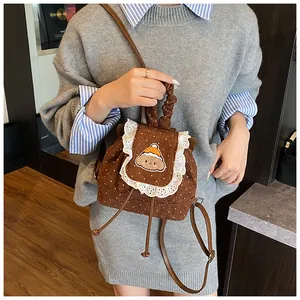 Détail du sac à dos en velours marron avec bordure en dentelle et broderie ours