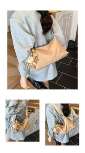 Détail du sac de messager beige avec breloque d'ours en peluche et logo brodé