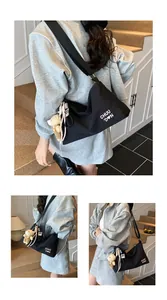 Détail du sac messager noir avec lettrage blanc, bandoulière large et breloque ours