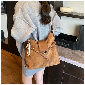 Details einer braunen Wildleder-Schultertasche mit Perlenanhänger und Metallösenriemen