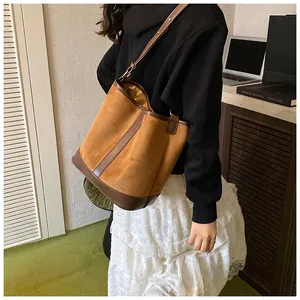 Brown patchwork bucket bag with suede texture shown on shoulder in a lifestyle setting