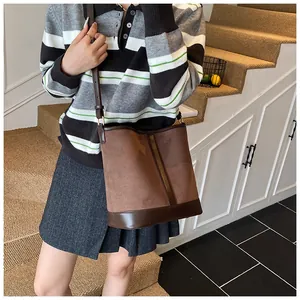 Detail view of large brown suede bucket bag with leather base worn by a model