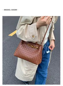 Detail of woven brown leather crossbody bag with gold chain strap on denim jeans