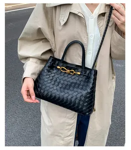 Detail of black woven leather bucket bag with gold knot buckle and woven strap
