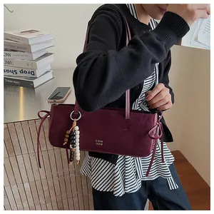 Detail of burgundy suede shoulder bag with beaded charm and gold logo lettering