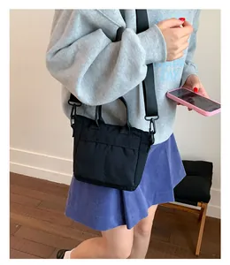 Detailaufnahme der schwarzen Umhängetasche mit Vordertasche an einem Model im grauen Hoodie