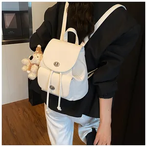 Detail eines weißen Lederrucksacks mit Kieselmaserung, Drehschloss und Plüschbär-Anhänger