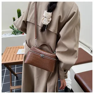 Detail of brown faux crocodile leather box bag with silver zippers and top handle