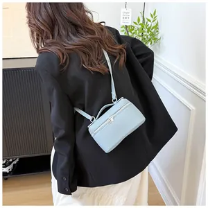 Sac bandoulière en cuir bleu clair à motif litchi porté sur une veste de costume