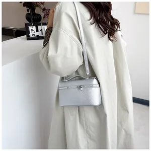 Détail d'un petit sac carré argenté à texture litchi porté à l'épaule par le mannequin