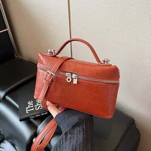 Brick red crocodile pattern box bag with top handle and crossbody strap held by hand