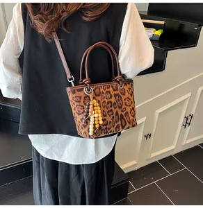 Detail of leopard print bucket bag featuring wooden bead tassel and brown round handle