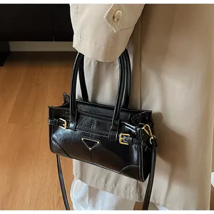 Close-up of black glossy leather handbag with gold metal hardware and adjustable strap
