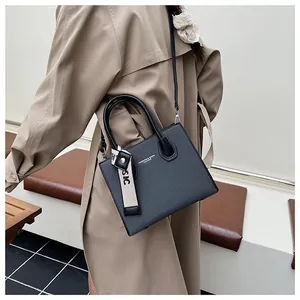 Detail of black leather square bag with gold lettering and decorative webbing strap