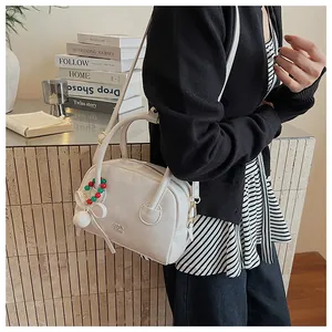 Détail du sac Boston blanc avec logo Cora et breloque festive avec nœud et perles