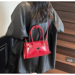Detail of red leather handbag with gold metal hardware and triangular plaque on front