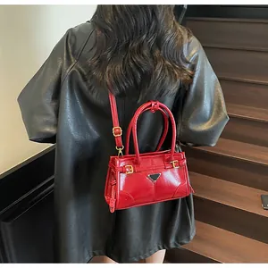 Glossy red faux leather handbag with triangle metal logo worn with a black coat