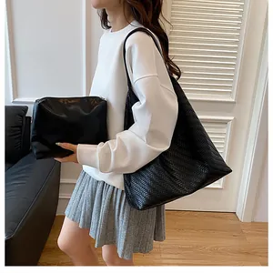 Detail of black woven shoulder tote bag and smooth clutch set held by a model