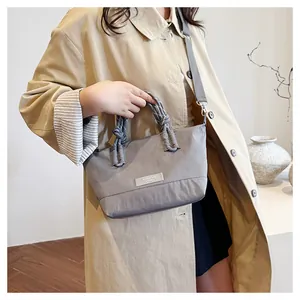 Grey nylon crossbody bag with double knot handles and adjustable shoulder strap worn with coat