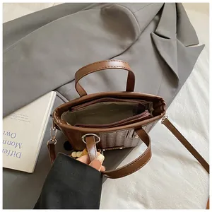 Braune gewebte Beuteltasche mit Henkeln und Perlenanhänger auf neutralem Stoff