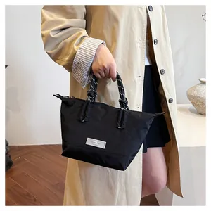 Detail of a black nylon shoulder bag with woven rope handle and silver metal nameplate
