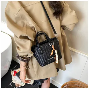 Detail einer schwarzen Web-Umhängetasche mit Perlenanhänger auf einem Trenchcoat