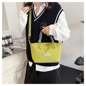 Detail of green nylon crossbody bag showing woven rope handles and a square fabric label