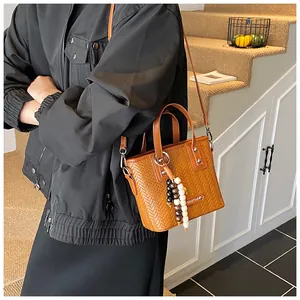 Detail einer braunen Web-Eimertasche mit Holzperlen und metallischem Logo-Anhänger