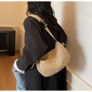 Detailed view of beige crossbody bag with adjustable strap worn by model against a wall