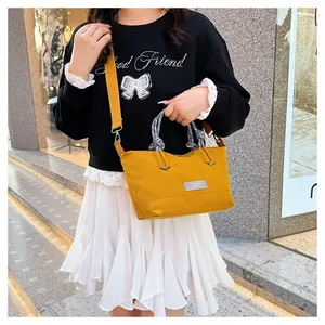 Detail of yellow canvas crossbody bag with rope handles held by a model in outdoor setting