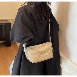 Detail of minimalist beige nylon crossbody bag worn on a black coat back for scale