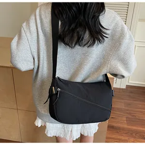 Detail of black nylon crossbody bag with diagonal zipper and adjustable strap on a model